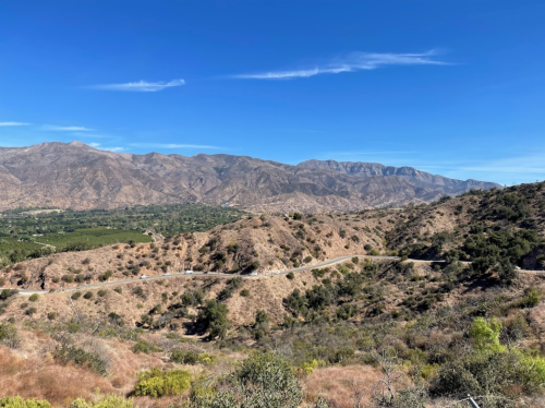 A scenic view of rolling hills and mountains under a clear blue sky, with a winding road in the foreground.