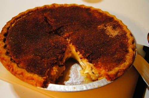 A freshly baked pie with a golden-brown crust and a slice removed, revealing a creamy filling inside.