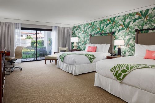 A bright hotel room with two beds, tropical wallpaper, and a balcony view. Modern decor and a cozy atmosphere.