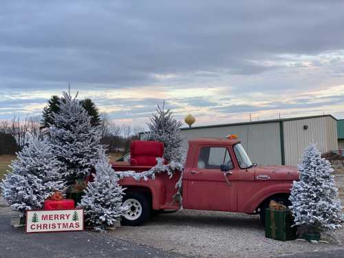 A vintage red truck decorated for Christmas, surrounded by snowy trees and festive gifts, with a "Merry Christmas" sign.