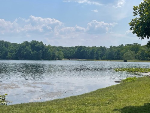 A serene lake surrounded by lush greenery and trees under a partly cloudy sky.