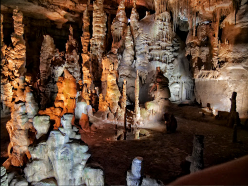 A stunning cave interior with colorful stalagmites and stalactites illuminated by various lights.