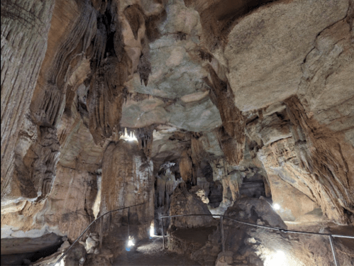 A dimly lit cave interior featuring rock formations and stalactites, with a pathway and lights illuminating the scene.