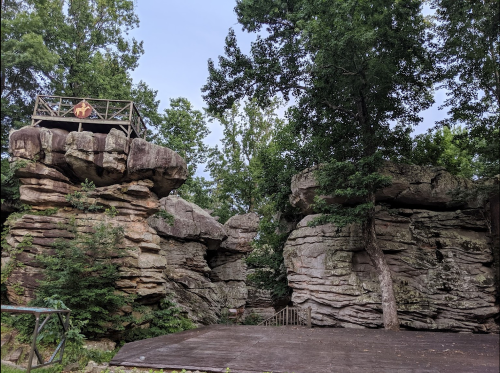 A rocky landscape with large boulders and a wooden platform surrounded by trees under a clear sky.