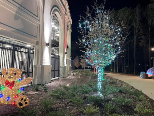 A decorated tree with blue and green lights beside a building, featuring a lit teddy bear in the foreground.