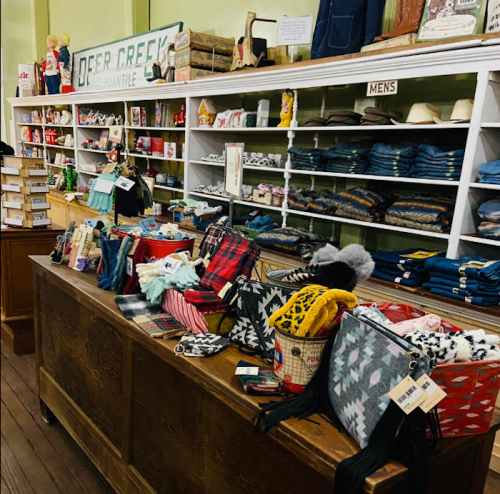 A cozy store display featuring clothing, accessories, and home goods on wooden tables and shelves.