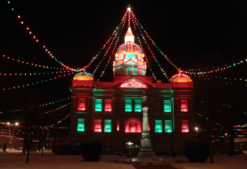 Historic building illuminated with red and green lights, adorned with festive decorations, during a winter night.