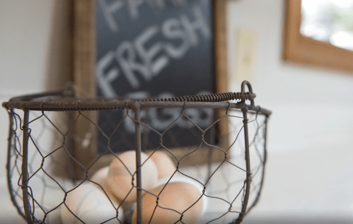 A wire basket with eggs in front of a chalkboard sign that reads "Fresh Eggs."