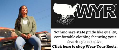 A smiling woman in a hoodie stands by an old truck, promoting state pride clothing with the text "Wear Your Roots."