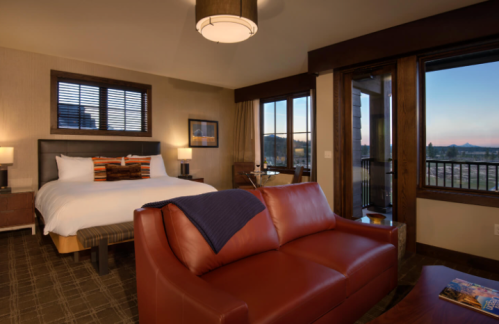 Cozy hotel room featuring a king bed, leather sofa, and large windows with scenic views.