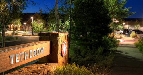 A wooden sign reading "Tetherow" at night, surrounded by trees and softly lit pathways.