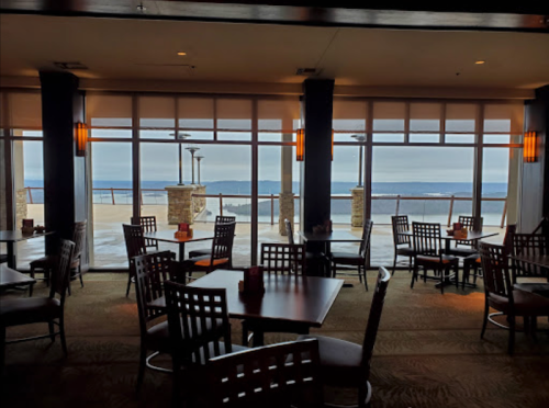 A cozy restaurant interior with wooden tables and chairs, featuring large windows overlooking a scenic view.