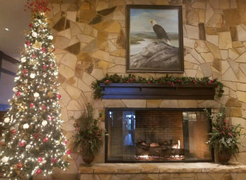 A cozy holiday scene featuring a decorated Christmas tree, a stone fireplace, and a painting of an eagle above the mantel.