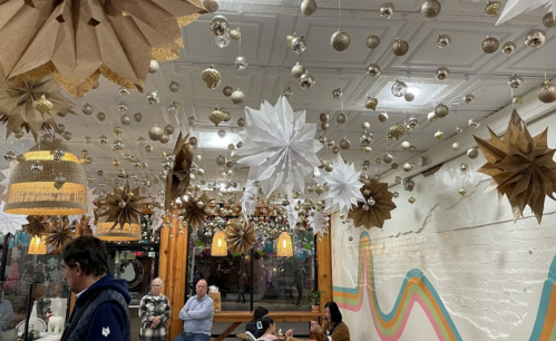 A cozy restaurant interior decorated with hanging paper stars and ornaments, featuring warm lighting and colorful wall accents.