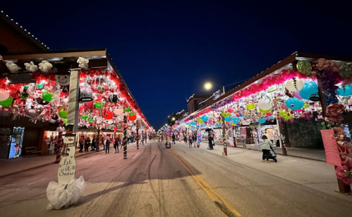 A festive street decorated with colorful lights and ornaments, bustling with people during the evening.