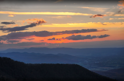 A vibrant sunset over rolling mountains, with colorful clouds and a valley below, creating a serene landscape.