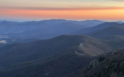 A panoramic view of rolling mountains at sunset, with soft hues of orange and purple in the sky.