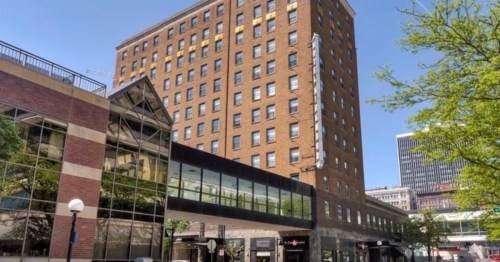 A tall brick building with large windows, connected to a modern glass structure, set against a clear blue sky.