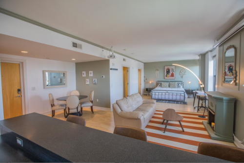 A modern living space featuring a sofa, dining area, bed, and stylish decor with large windows and natural light.