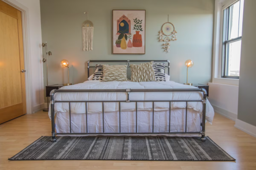 A stylish bedroom featuring a metal bed frame, decorative pillows, and wall art, with warm lighting and a cozy rug.