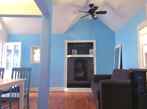 Bright room with blue walls, a fireplace, a brown couch, and a dining table with blue chairs.