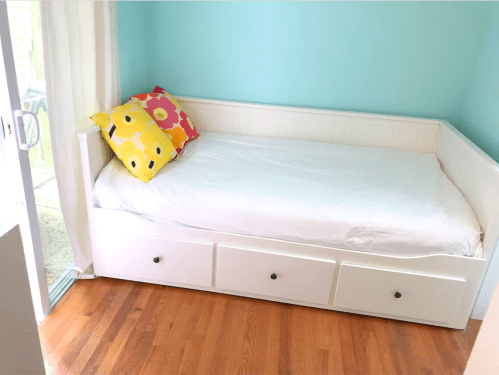 A bright room with a white daybed, colorful flower-patterned pillows, and light blue walls.
