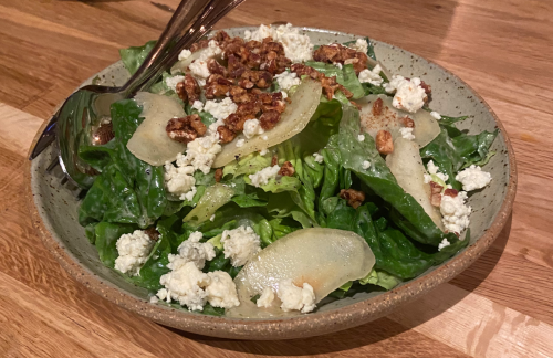 A bowl of fresh salad with romaine lettuce, sliced pears, crumbled cheese, and walnuts on a wooden table.