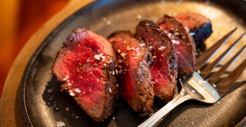 Sliced medium-rare steak on a black plate, garnished with coarse salt, next to a fork.
