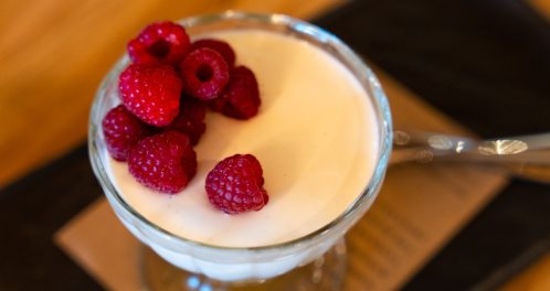 A glass dessert cup filled with creamy yogurt topped with fresh raspberries.