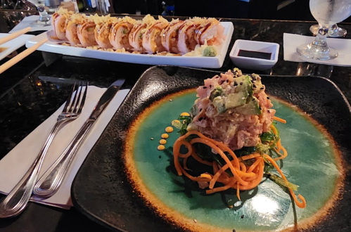 A plate of sushi rolls in the background and a colorful dish with seafood and vegetables in the foreground.