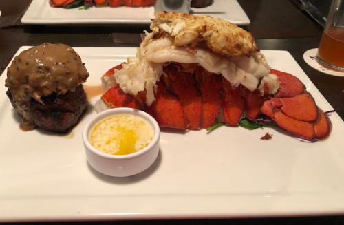 A gourmet plate featuring lobster tail, crab meat, a beef filet with gravy, and melted butter on the side.