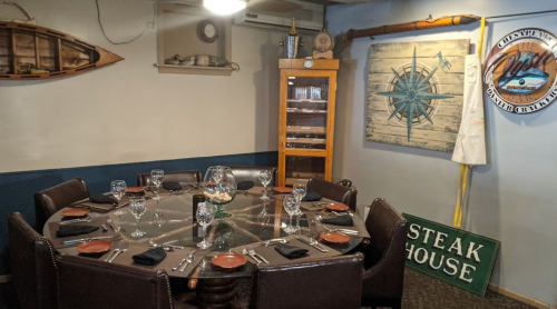 A cozy restaurant dining area with a round table set for eight, nautical decor, and a steakhouse sign.