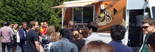 A crowd of people waiting in line at a food truck on a sunny day.