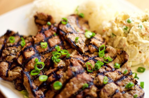 Grilled meat served with rice and a creamy potato salad, garnished with chopped green onions.