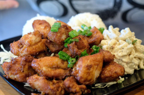 A plate of crispy fried chicken pieces topped with green onions, served with rice and macaroni salad.