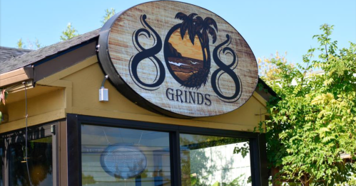 Sign for "808 Grinds" featuring palm trees and a sunset, set against a clear blue sky.