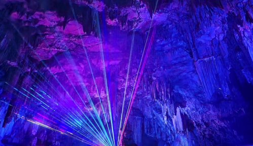 Colorful laser lights illuminate a stunning cave interior with vibrant purple and blue hues.