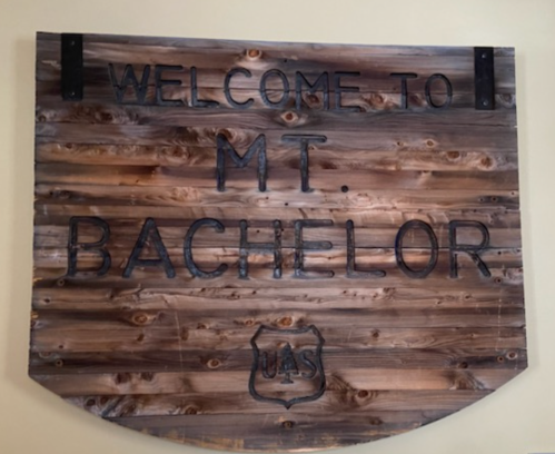 Wooden sign reading "Welcome to Mt. Bachelor" with a shield emblem below.