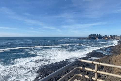 A scenic view of the ocean with waves crashing against rocky shores under a clear blue sky.