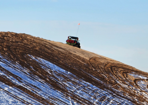 A vehicle climbs a sandy hill with a blue sky in the background, showcasing tire tracks in the sand.