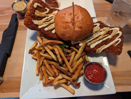 A plate featuring two crispy fried chicken fillets, a burger bun, and a side of golden French fries with ketchup.