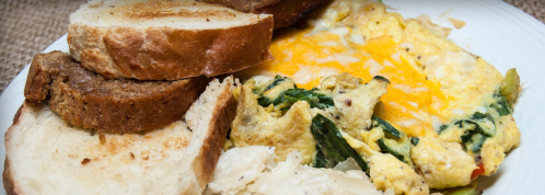 A plate with two slices of toasted bread, a cheesy spinach omelet, and a side of hash browns.