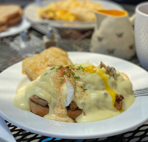 A plate of eggs Benedict with hollandaise sauce, served on toasted bread, with a side of hash browns.