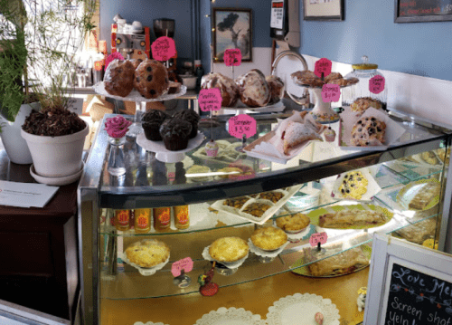 A display case filled with various baked goods, including muffins, cupcakes, and pastries, with price tags visible.