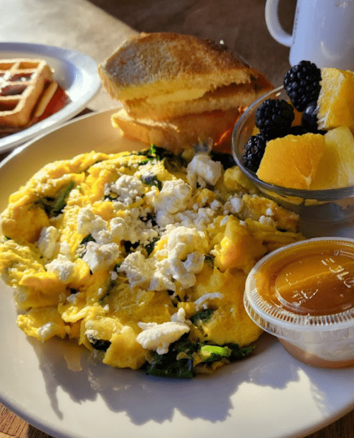 A plate with a spinach and feta omelette, toast, fruit cup, and a small container of honey.