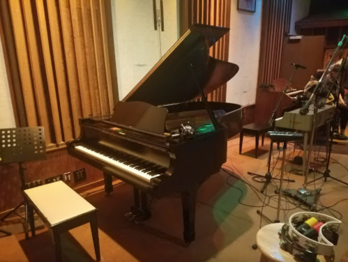 A grand piano in a music studio, with microphones and music stands nearby, set in a warm, inviting atmosphere.