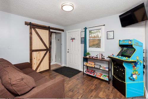 Cozy game room with a brown couch, arcade machine, and a sliding barn door leading to another room.