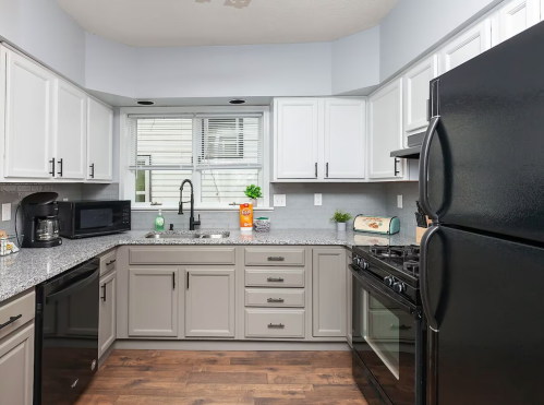 Modern kitchen with gray cabinets, black appliances, and a window above the sink, featuring a granite countertop.