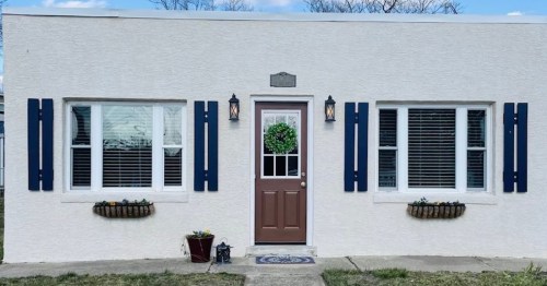 A white house with blue shutters, a brown door, and flower boxes under the windows, featuring a wreath on the door.