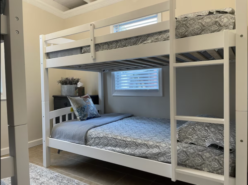 A white bunk bed with a patterned comforter in a well-lit room featuring a window and decorative pillows.